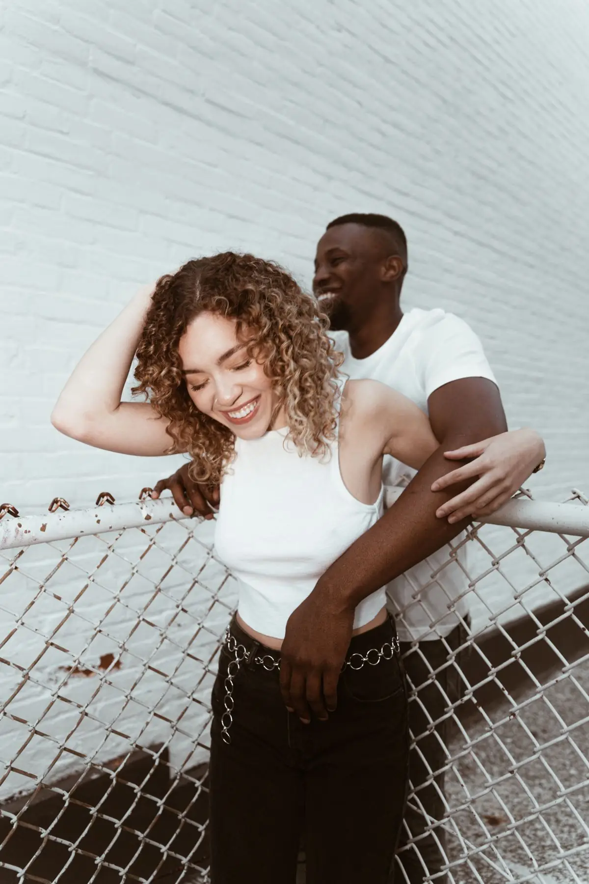 A laughing couple leaning on a fence by a white wall